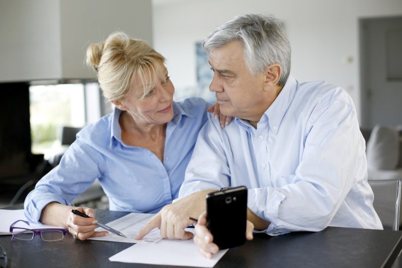 Senior couple checking accounts with smartphone in house