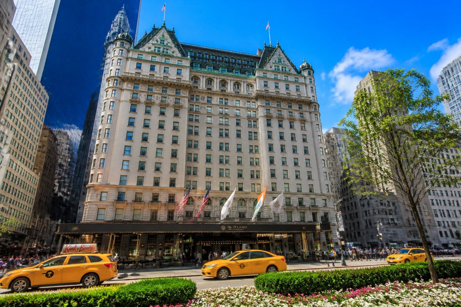 The exterior of The Plaza hotel in New York City with people walking and taxis passing on the street in front.