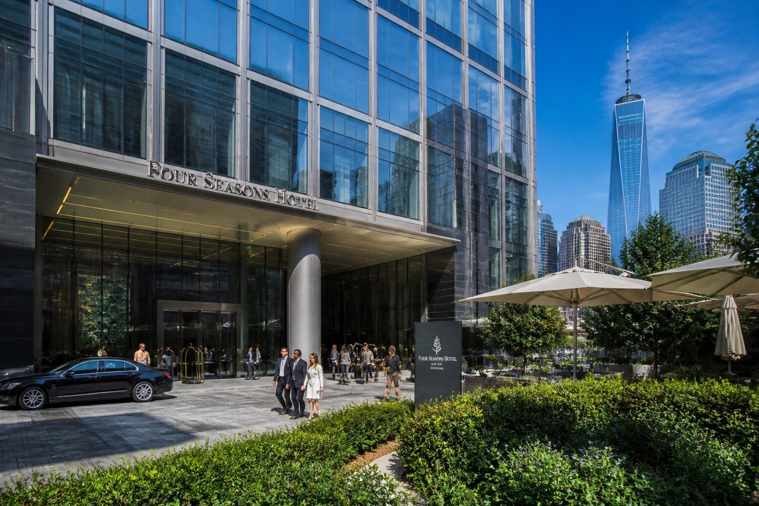 Exterior view of the Four Seasons Hotel New York Downtown with guests and staff near the entrance on a sunny day.