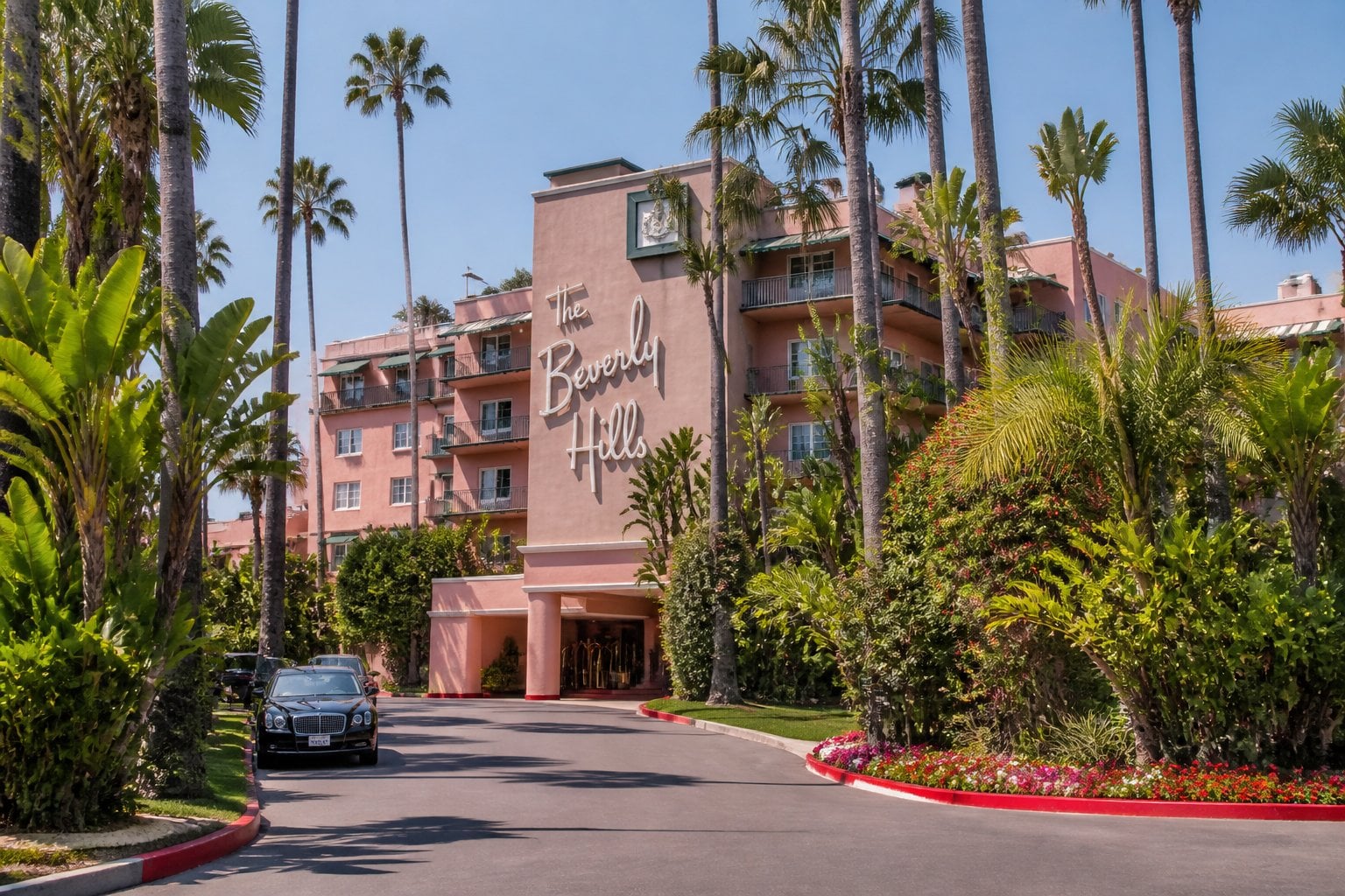 The Beverly Hills Hotel entrance with pink building, palm trees, and luxury cars on a sunny day.