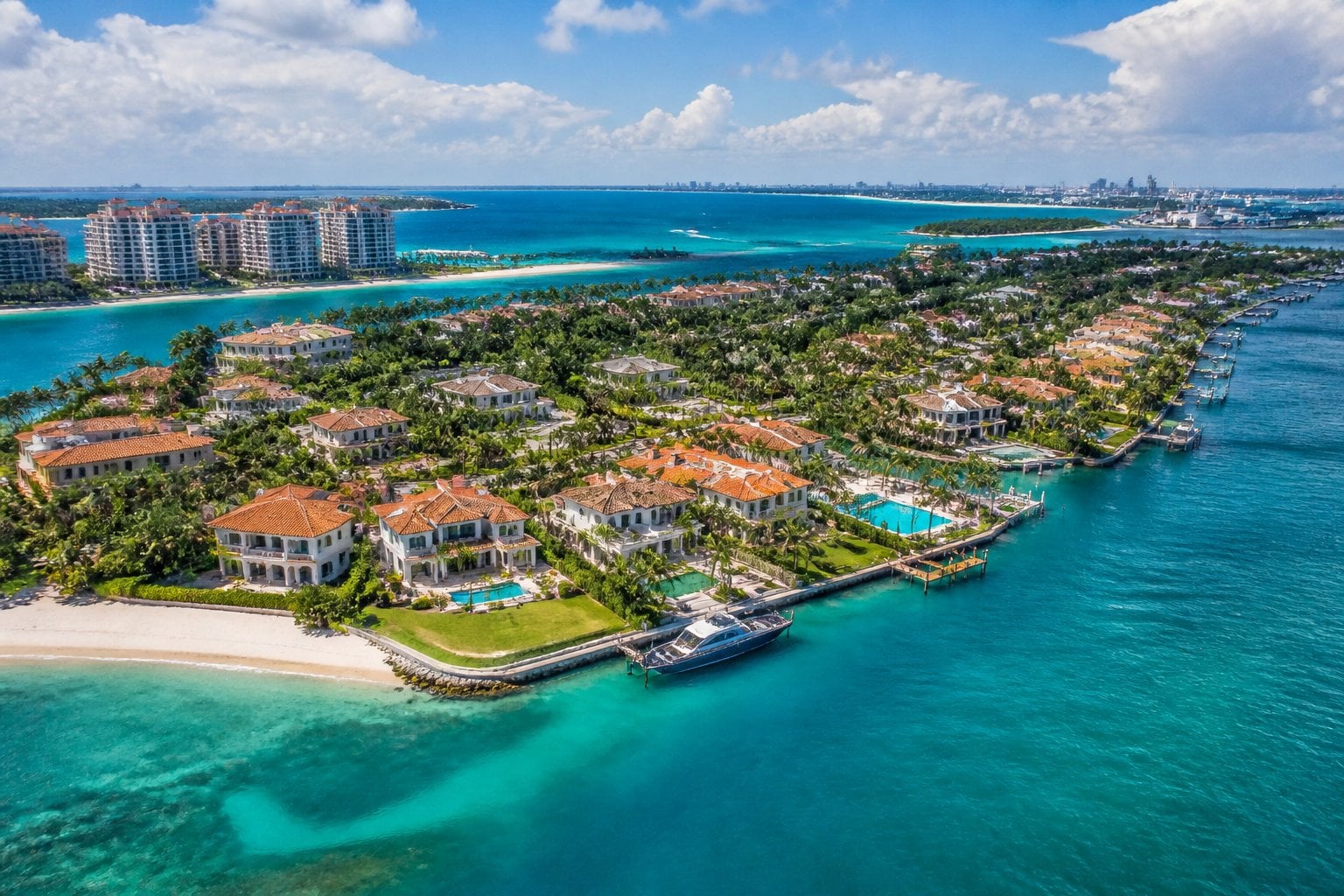 Aerial view of Fisher Island in Miami with luxury waterfront homes, sandy beaches, and clear blue ocean water under a sunny sky.