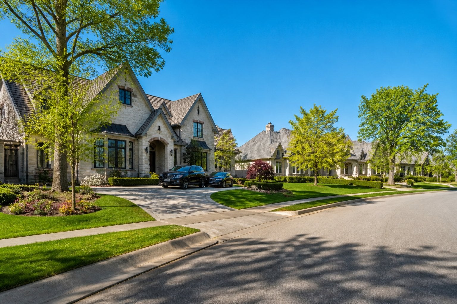 A quiet, upscale suburban neighborhood with large houses, green lawns, and trees under a clear blue sky.