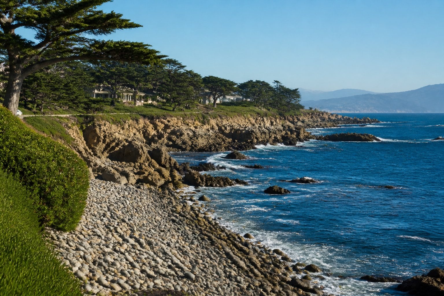 Rocky coastline with pebbles, pine trees, and clear blue ocean under a bright sky at Pebble Beach, California.