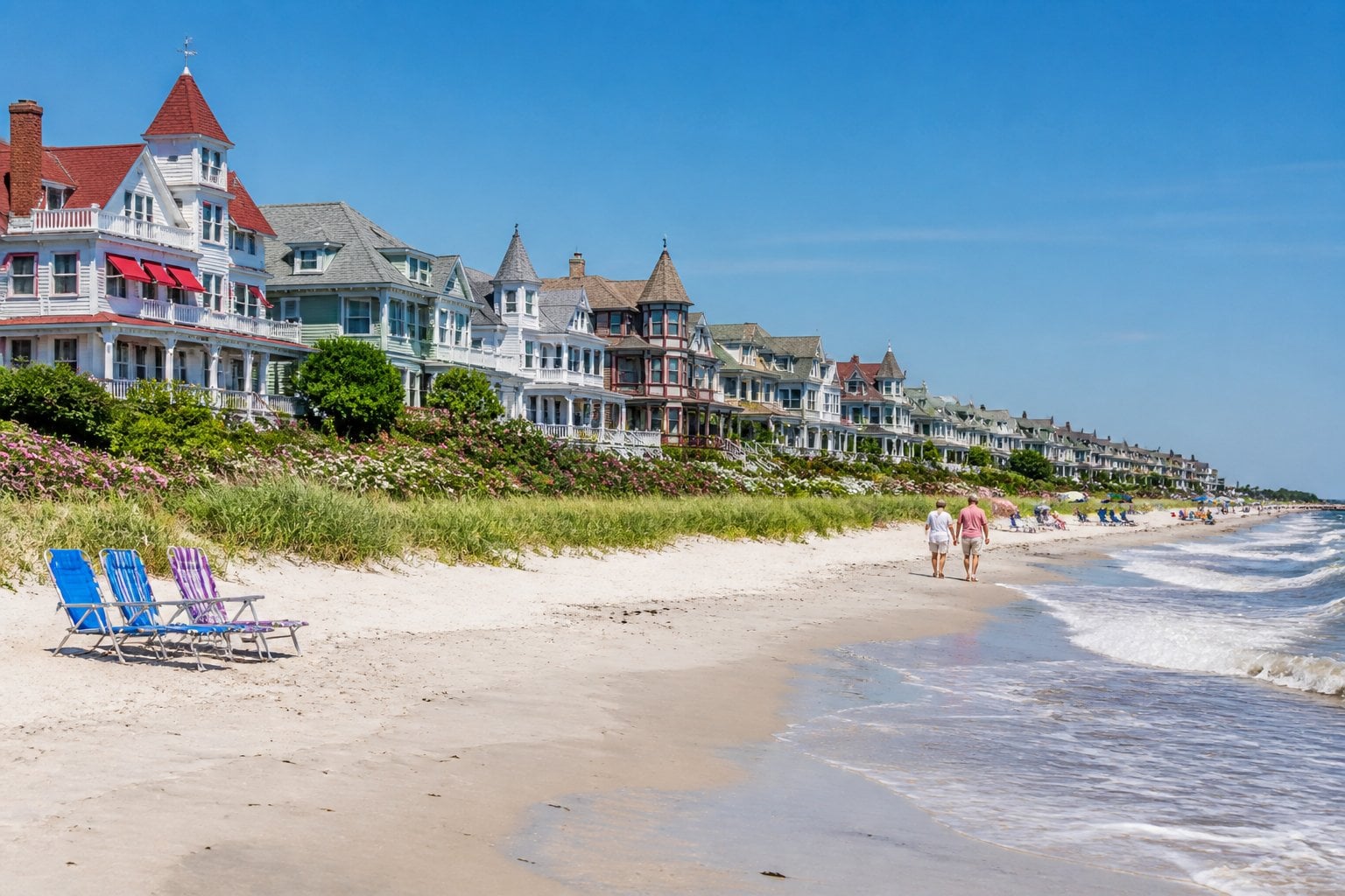 A sandy beach with gentle waves, colorful Victorian houses along the shore, and people enjoying a sunny day in Cape May, New Jersey.