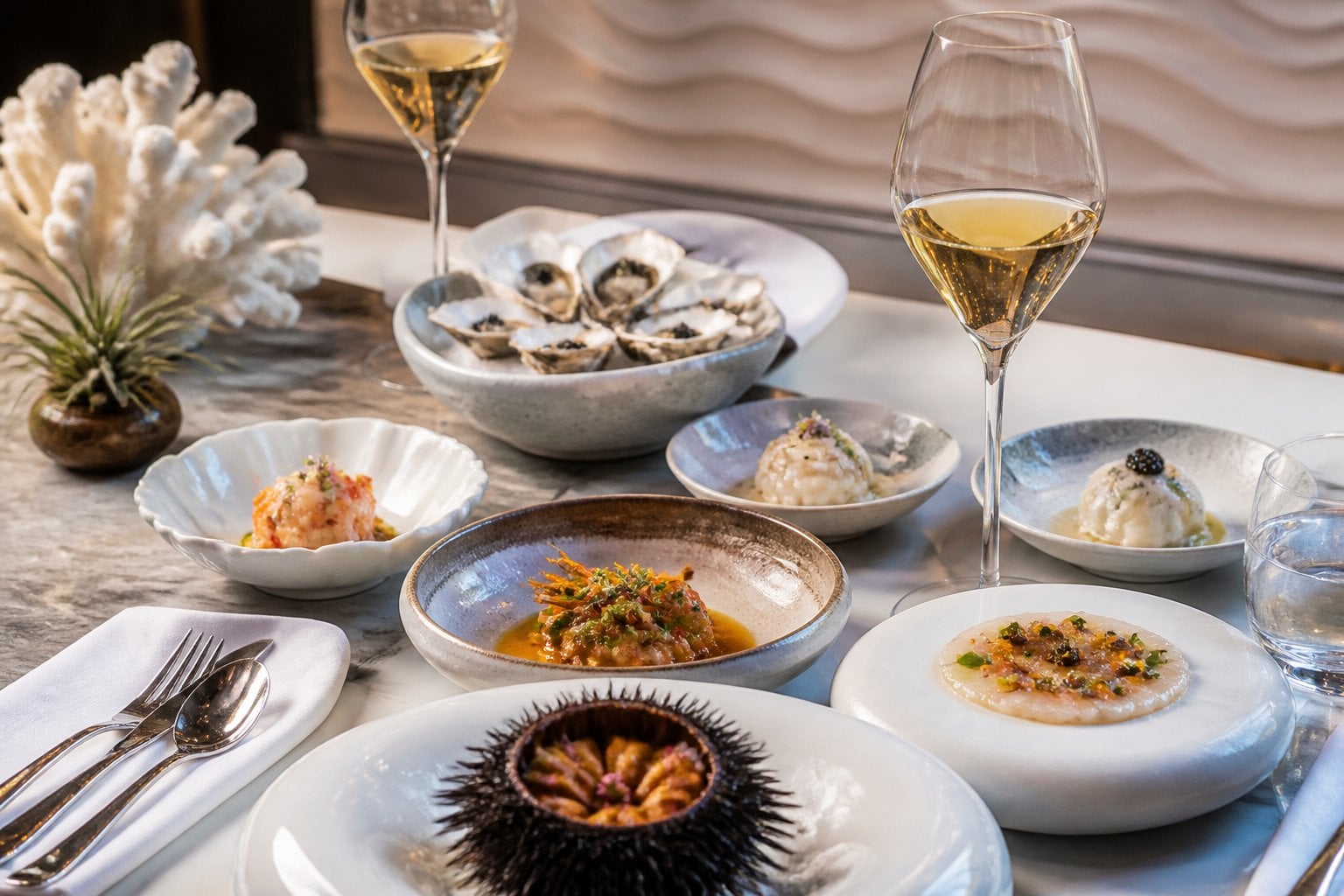 A table set with multiple small plates of artfully presented seafood dishes, fine glassware, and silverware in an elegant restaurant setting.