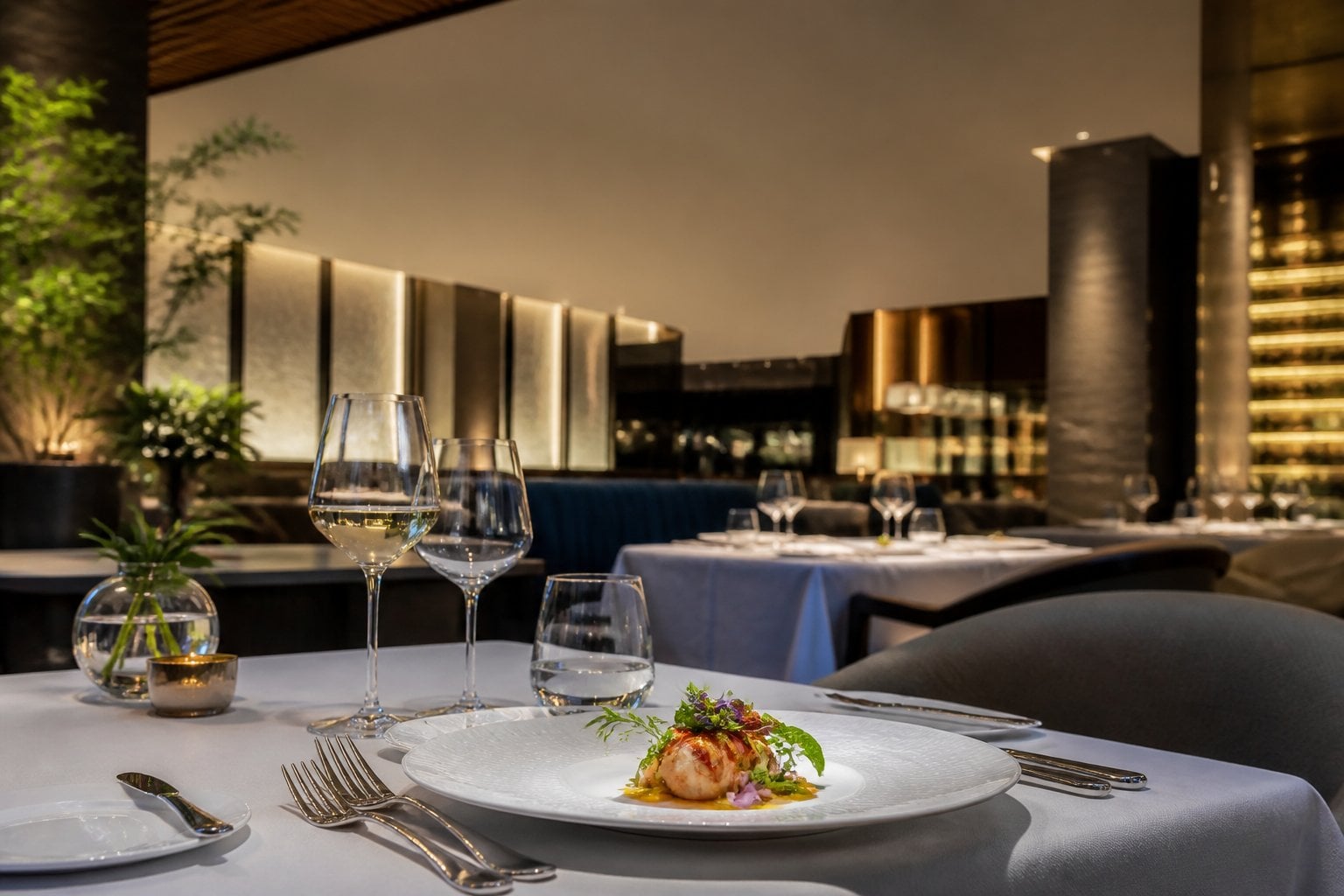 An elegant luxury restaurant table set with fine china, silverware, crystal glasses, and an artistic plated dish.